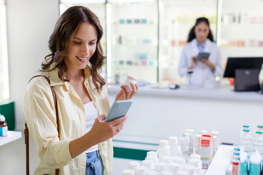 woman using cellphone and holding jar of pills and looking for information of medicine in drugstore